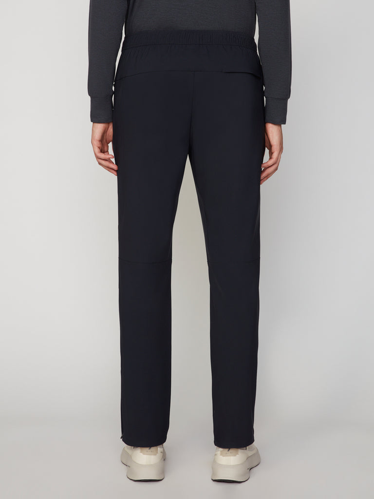 A person stands facing away from the camera in a dark long-sleeve top, TECH APPAREL MEN’S PULL-ON TRAINING PANT RELAXED TAPERED FIT, and light sneakers against a plain background—highlighting athletic versatility.