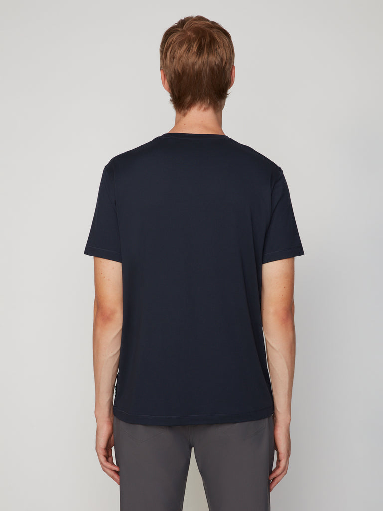 A person with short light brown hair stands with their back to the camera, wearing a TECH APPAREL MEN’S PEACH:TECH CLASSIC FIT CREW NECK T-SHIRT in dark navy and gray pants against a light gray background.