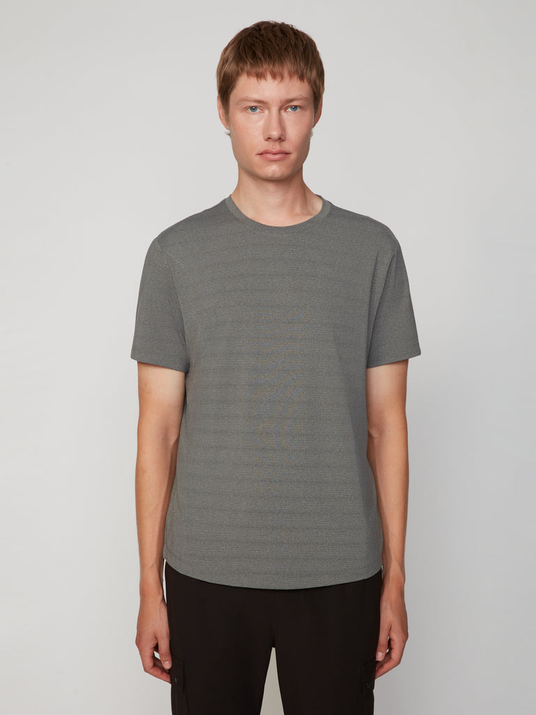 A person with short light brown hair wears the TECH APPAREL MEN’S CREW NECK TEE WITH MIXED JACQUARD STRIPE in gray and black pants, standing against a plain light background to showcase its lightweight comfort.
