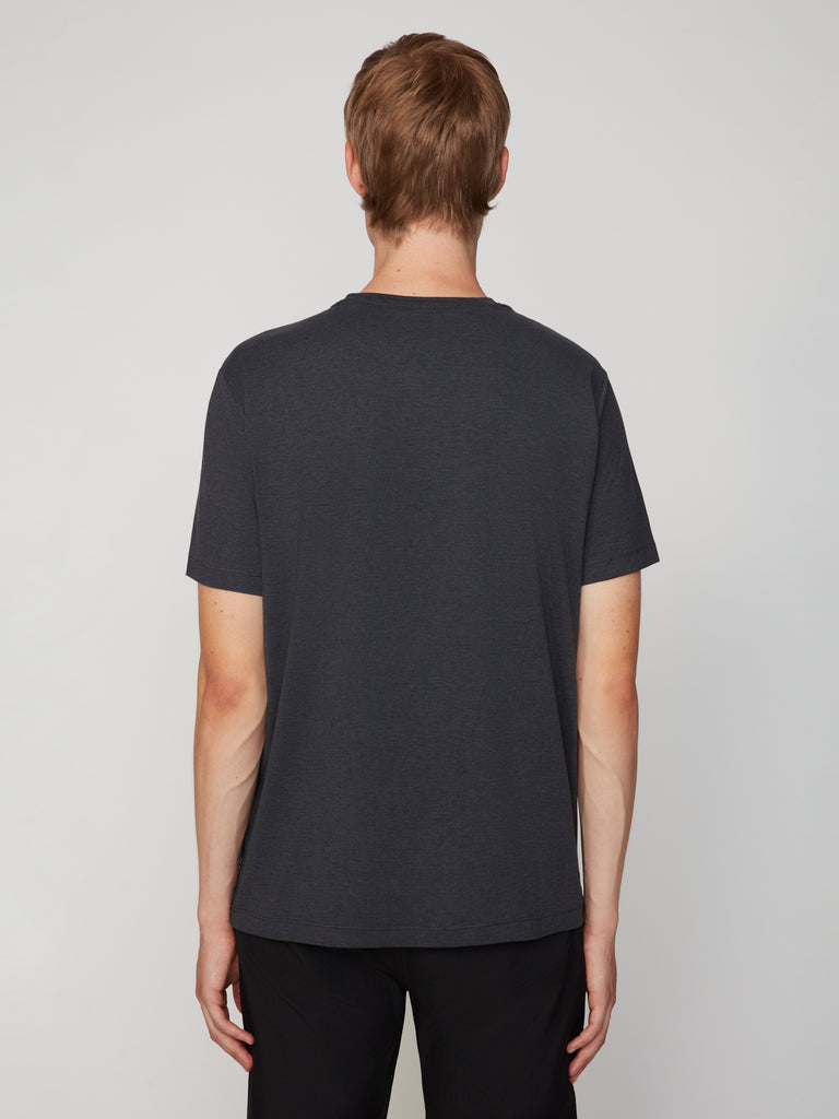 A person with short light brown hair, facing away from the camera, wears black pants and a TECH APPAREL MEN’S CREW NECK T-SHIRT IN BRUSHED SPACE-DYED JERSEY against a light gray background.