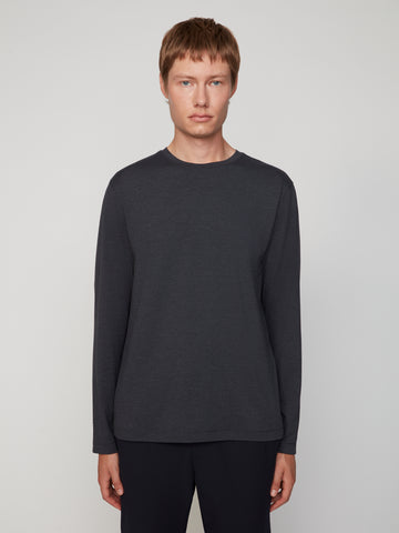 A person with short light brown hair wears TECH APPAREL’s MEN’S LONG SLEEVE CREW NECK IN BRUSHED SPACE-DYED JERSEY and black pants, standing against a plain light background.
