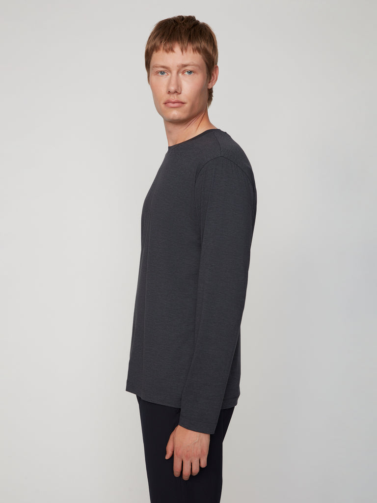 A man with short light brown hair models the TECH APPAREL MEN’S LONG SLEEVE CREW NECK IN BRUSHED SPACE-DYED JERSEY in dark gray, standing sideways and facing the camera against a plain light gray background.