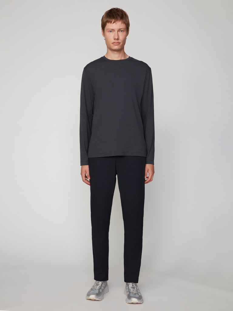 A person with short light brown hair wears TECH APPARELs MEN’S LONG SLEEVE CREW NECK IN BRUSHED SPACE-DYED JERSEY, black pants, and gray sneakers, standing facing forward against a plain light gray background.