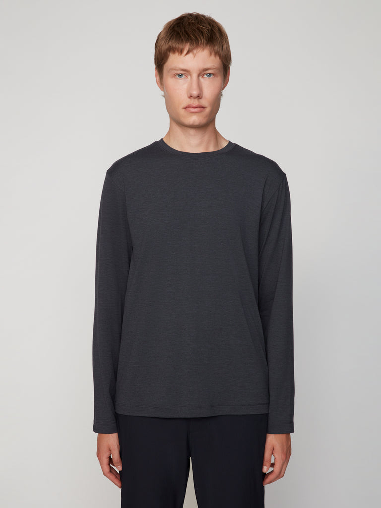 A young person with short, light brown hair models the TECH APPAREL MEN’S LONG SLEEVE CREW NECK IN BRUSHED SPACE-DYED JERSEY and black pants, standing against a plain light grey background for breathable warmth and comfort.