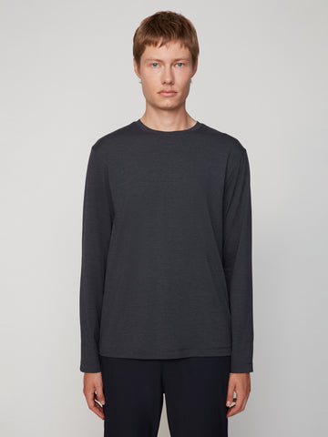 A young person with short, light brown hair models the TECH APPAREL MEN’S LONG SLEEVE CREW NECK IN BRUSHED SPACE-DYED JERSEY and black pants, standing against a plain light grey background for breathable warmth and comfort.