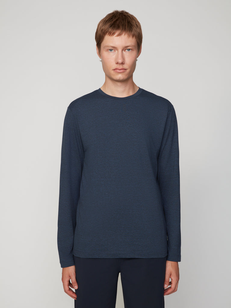 A young person with short light brown hair wears the TECH APPAREL MEN’S LONG SLEEVE CREW NECK IN BRUSHED SPACE-DYED JERSEY and dark pants, standing against a plain light gray background, facing forward with a neutral expression.