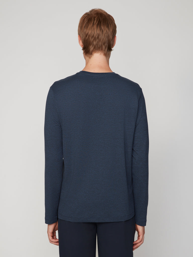 A person with short light brown hair, wearing the TECH APPAREL MEN’S LONG SLEEVE CREW NECK IN BRUSHED SPACE-DYED JERSEY and dark pants, stands facing away from the camera against a plain light gray background.