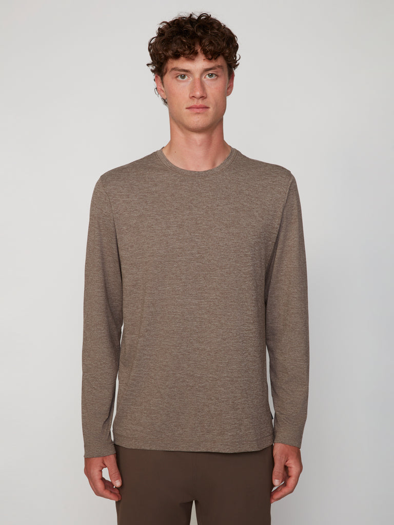 A young man with curly brown hair stands facing forward, wearing the TECH APPAREL MEN’S LONG SLEEVE CREW NECK IN BRUSHED SPACE-DYED JERSEY in light brown and matching pants, set against a plain light gray background.