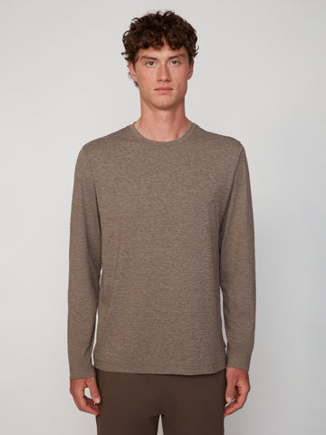 A young man with curly brown hair stands facing forward, wearing the TECH APPAREL MEN’S LONG SLEEVE CREW NECK IN BRUSHED SPACE-DYED JERSEY in light brown and matching pants, set against a plain light gray background.