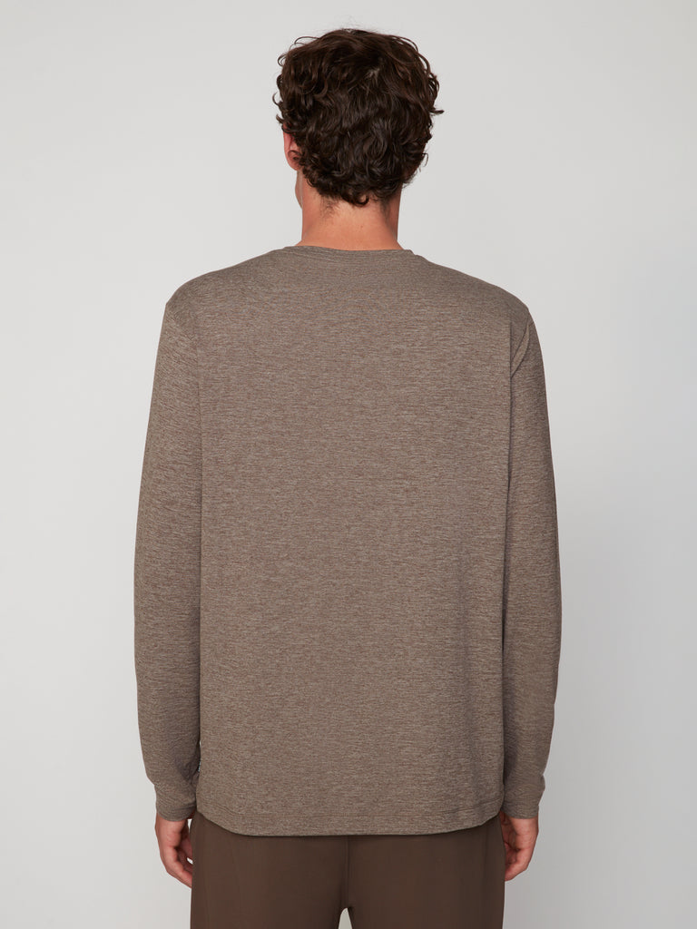 Seen from behind, a person with short, curly brown hair wears TECH APPAREL’s MEN’S LONG SLEEVE CREW NECK IN BRUSHED SPACE-DYED JERSEY in taupe and brown breathable performance pants against a plain light background.