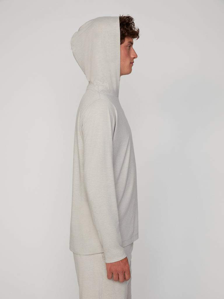 A person in profile wears the TECH APPAREL MEN’S LONG SLEEVE HOODIE IN BRUSHED SPACE-DYED JERSEY with the hood up and matching pants, providing breathable warmth against a plain light background.