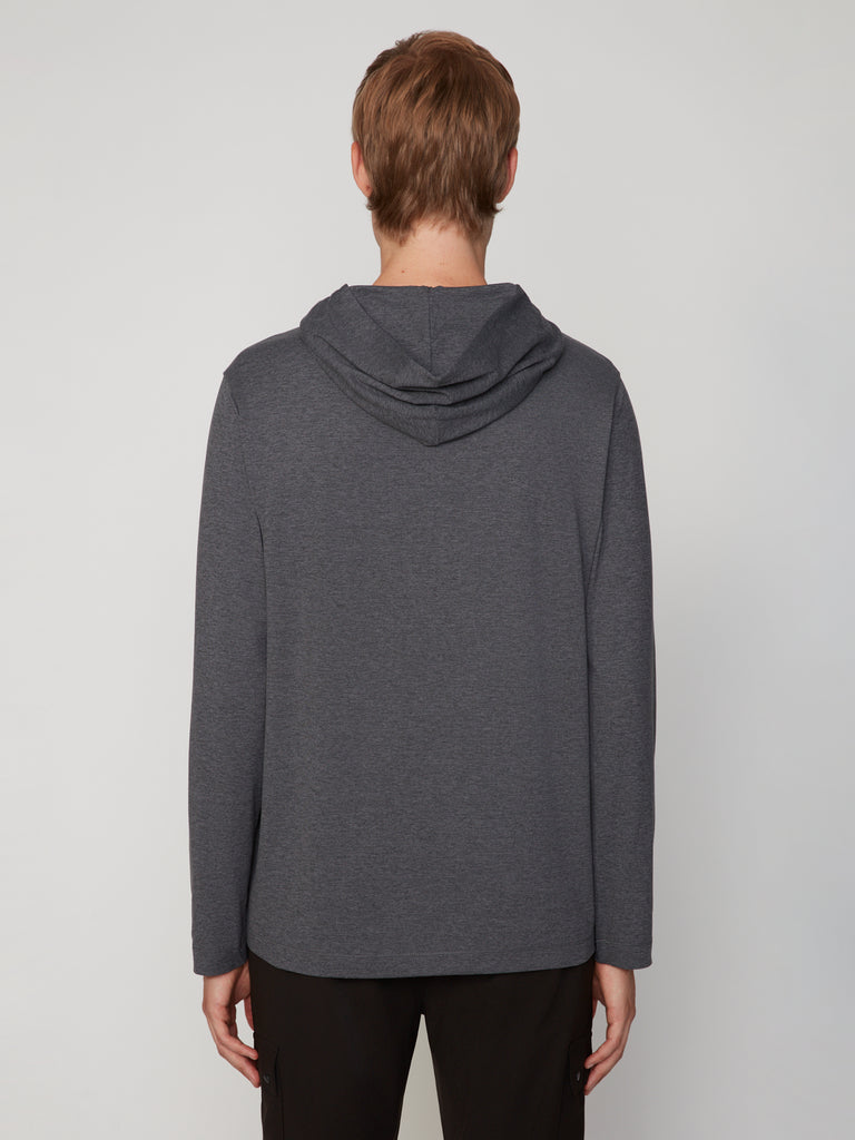 A person with short light brown hair is seen from behind, wearing the TECH APPAREL MEN’S LONG SLEEVE HOODIE IN BRUSHED SPACE-DYED JERSEY and black pants, set against a plain light gray background.