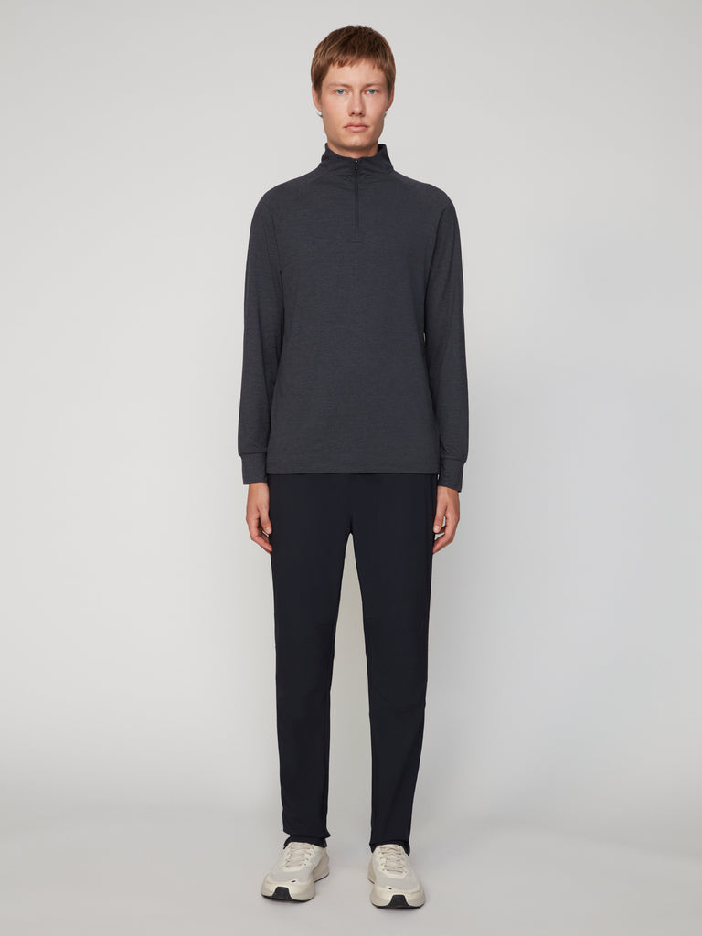 A person stands facing forward against a plain light gray background, wearing the TECH APPAREL MEN’S 1/4 ZIP MOCK NECK LONG SLEEVE IN BRUSHED SPACE-DYED JERSEY, matching dark pants, and white sneakers.