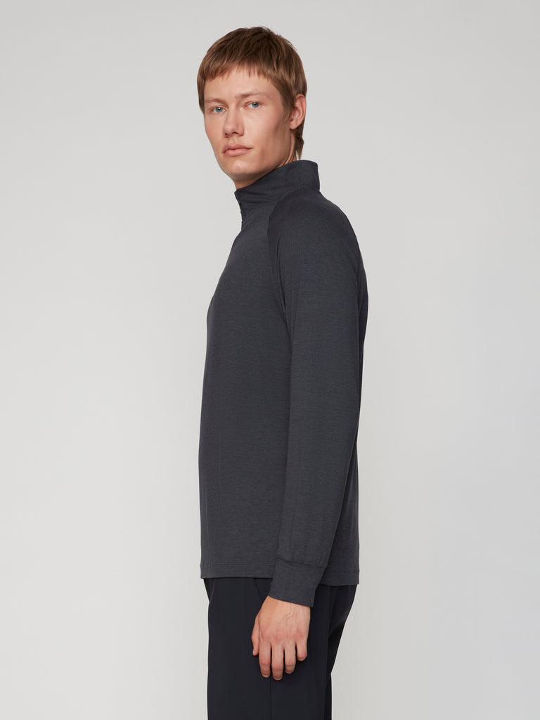 A man with short light brown hair stands sideways against a plain light background, wearing the TECH APPAREL MEN’S 1/4 ZIP MOCK NECK LONG SLEEVE IN BRUSHED SPACE-DYED JERSEY.