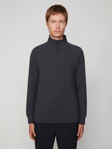 A man with short light brown hair wears the TECH APPAREL MEN’S 1/4 ZIP MOCK NECK LONG SLEEVE IN BRUSHED SPACE-DYED JERSEY in dark gray and dark pants, standing against a plain light gray background, facing forward neutrally.