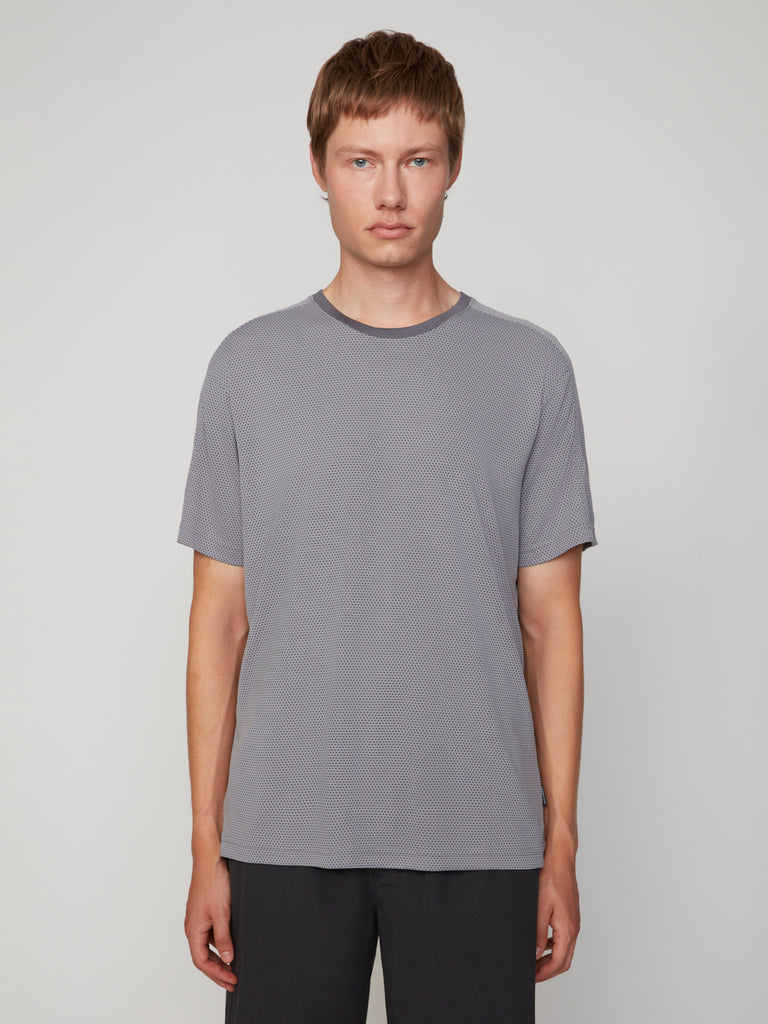 A young person with short light brown hair faces forward, wearing a TECH APPAREL MEN’S EYELET JACQUARD CREW NECK T-SHIRT in gray and dark pants against a plain light background.