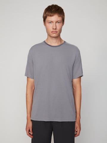 A young person with short light brown hair faces forward, wearing a TECH APPAREL MEN’S EYELET JACQUARD CREW NECK T-SHIRT in gray and dark pants against a plain light background.