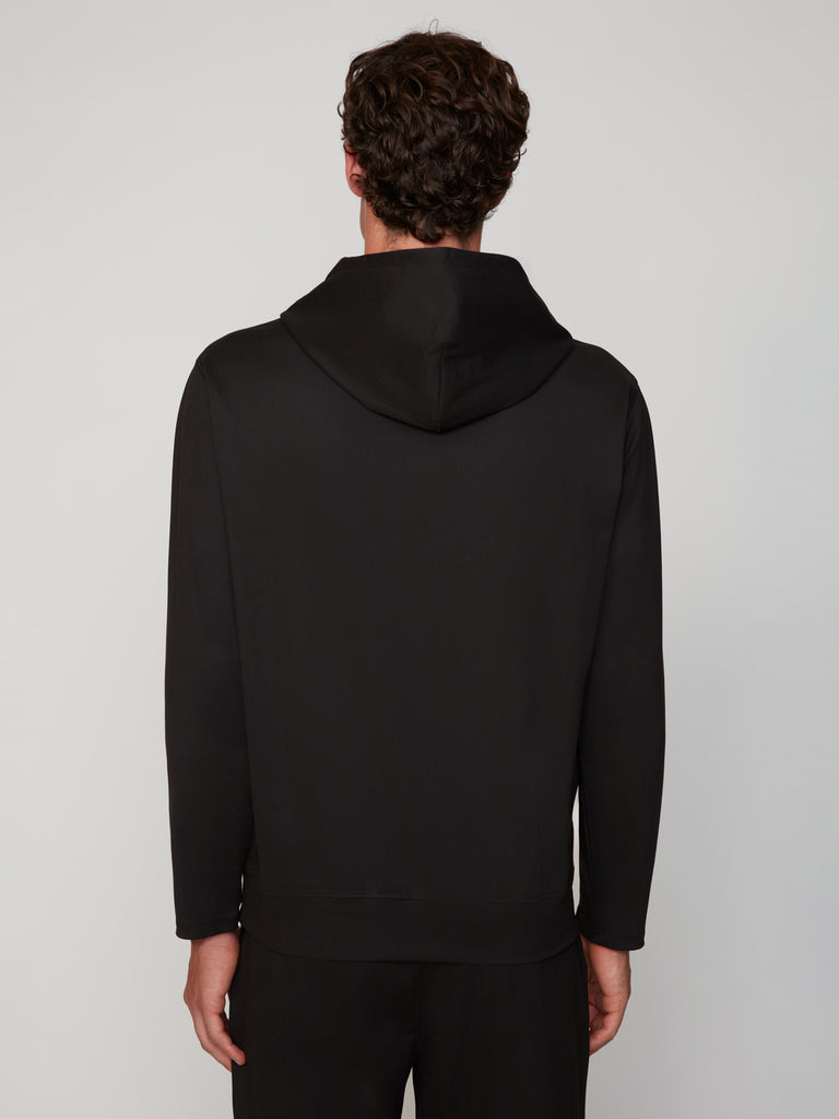 A man with short, curly brown hair is seen from behind wearing TECH APPAREL’s MEN’S FLEXURA FULL-ZIP MOCK NECK – LONG SLEEVE in black, paired with black pants, against a plain light gray background.