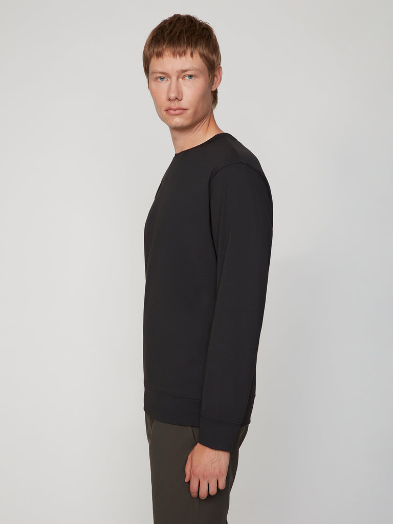 A young man with short brown hair models the TECH APPAREL MEN’S TECH:SOFT CLASSIC FIT LONG SLEEVE PULL-OVER, standing slightly to the side against a plain light background, showcasing its breathable warmth.
