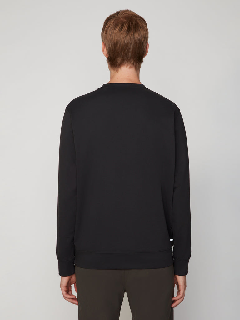 A person with short, light brown hair faces away from the camera, wearing the TECH APPAREL MEN’S TECH:SOFT CLASSIC FIT LONG SLEEVE PULL-OVER and dark pants against a light gray background.