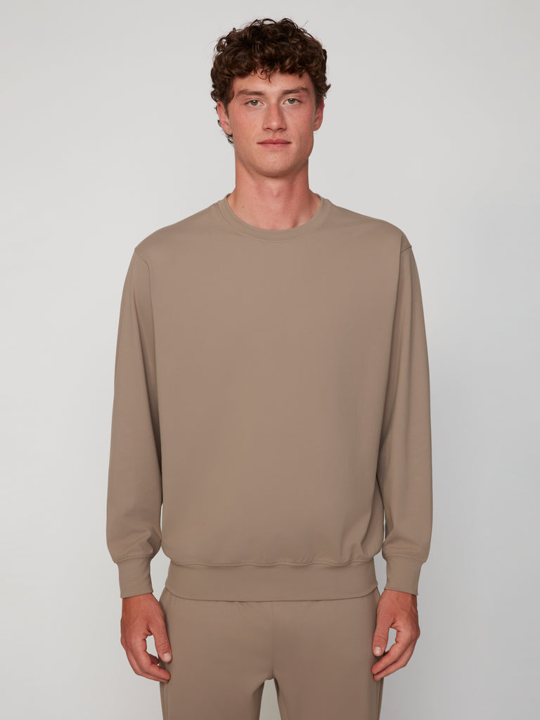A young man with short curly hair faces forward, wearing the TECH APPAREL MEN’S TECH:SOFT CLASSIC FIT LONG SLEEVE PULL-OVER for breathable warmth, paired with matching pants against a plain light background.
