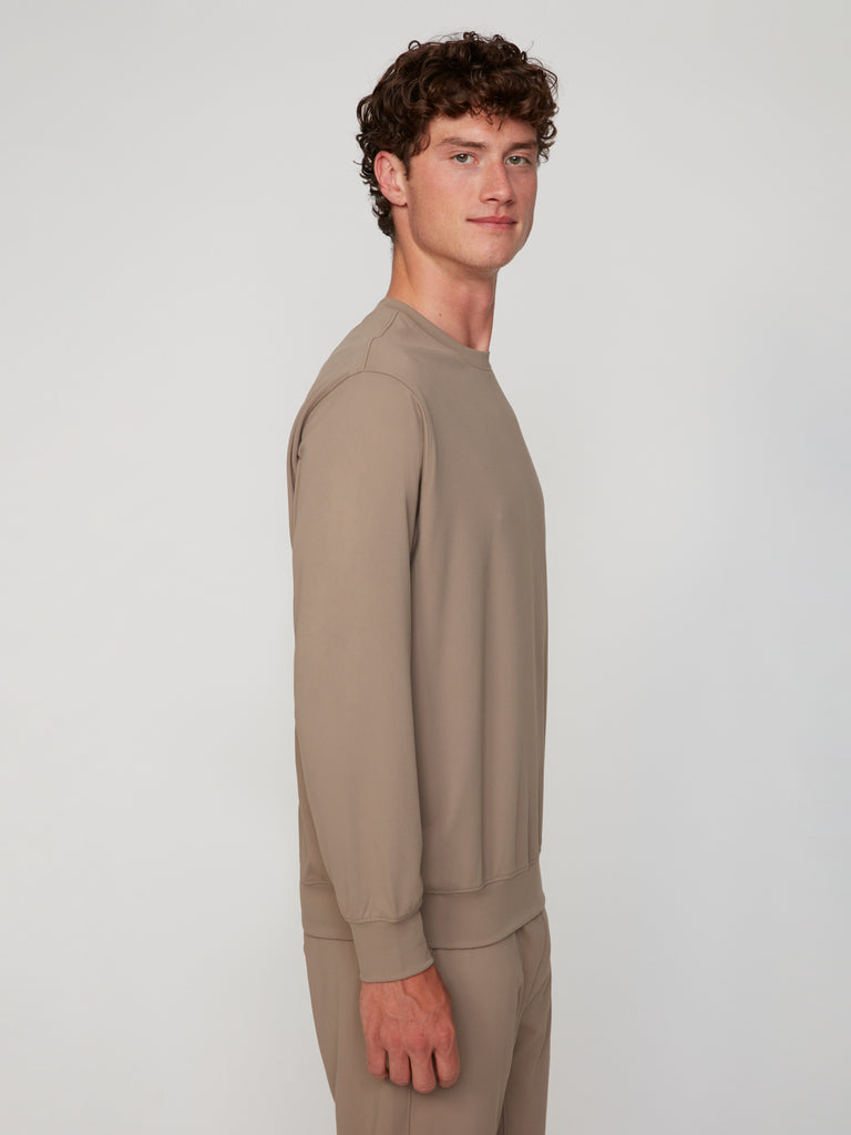 A young man with curly brown hair stands sideways against a light gray background, wearing the TECH APPAREL MEN’S TECH:SOFT CLASSIC FIT LONG SLEEVE PULL-OVER and matching pants, looking slightly toward the camera with a neutral expression.