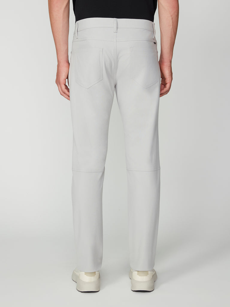 A person is shown from the back against a plain light background, wearing TECH APPAREL MENS FLUX 2.0 5-POCKET PANT in light gray stretch fabric with back pockets, paired with a black top and white shoes. The pants are wrinkle-resistant.