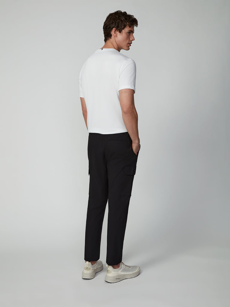 A man models the TECH APPAREL MENS FLUX 2.0 PULL-ON CARGO PANT, paired with a white short-sleeve shirt and sneakers, posing against a plain light background while looking over his shoulder.