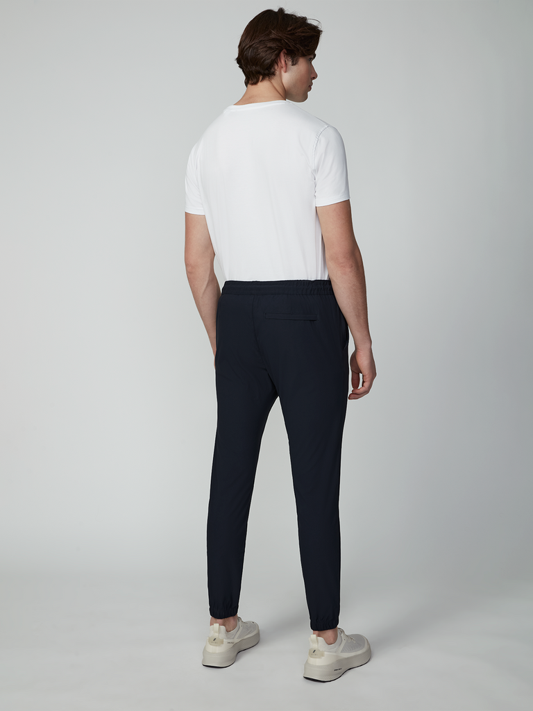 A man stands facing away, wearing a white t-shirt, white sneakers, and TECH APPAREL MENS DRI-FLEX JOGGER in dark navy, against a plain light background.