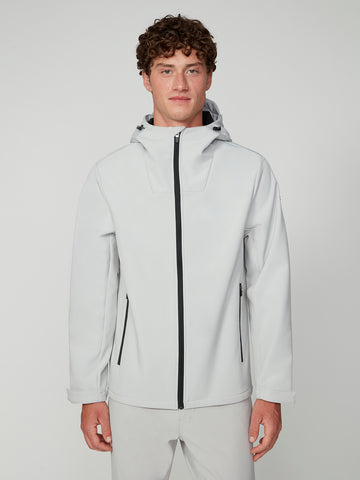 A young man with curly brown hair models the TECH APPAREL MENS BONDED FLEECE JACKET in light gray, featuring black zippers and a modern design. He stands facing the camera against a plain light background, hands by his sides.