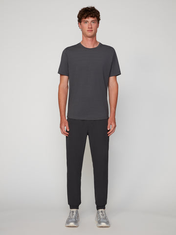 A young man stands against a light background wearing TECH APPAREL MEN’S 360:FLEX CLASSIC FIT PULL-ON CHINO JOGGER in dark gray, paired with a matching tee and gray sneakers for a comfortable, modern look.