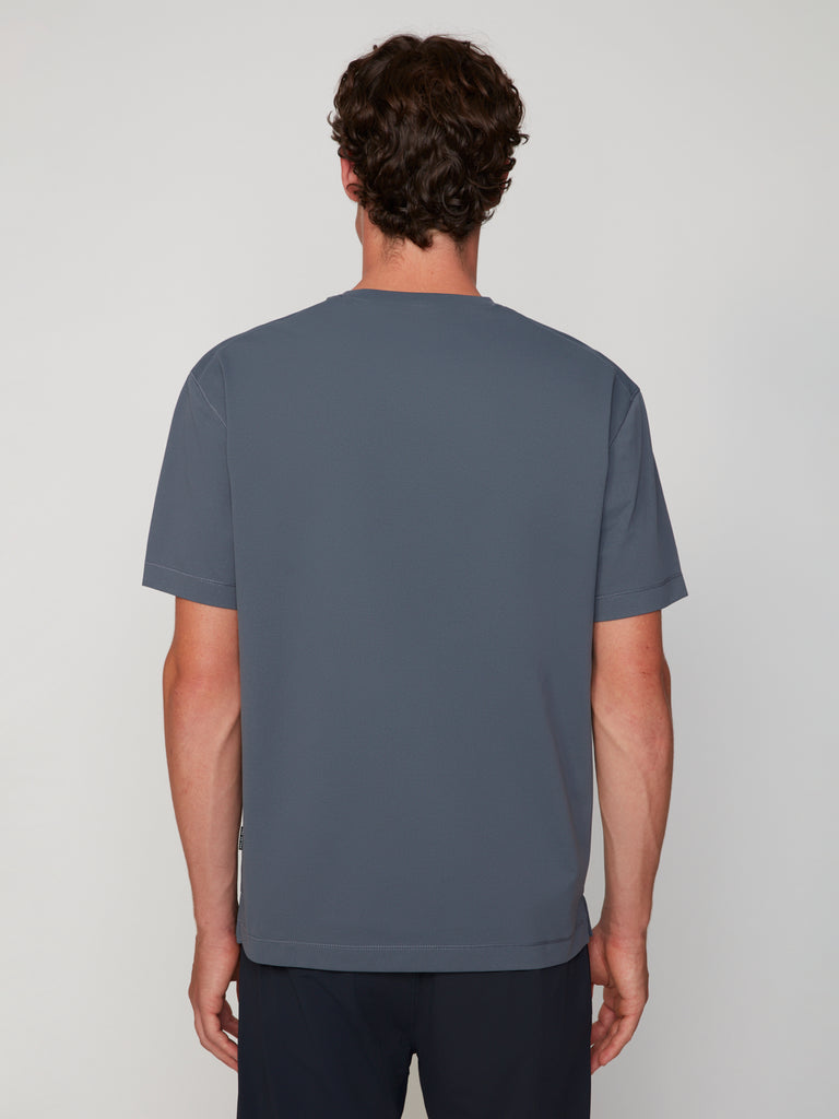 A man with short brown hair faces away from the camera, wearing TECH APPARELs MEN’S PURE FEEL RELAXED DROP SHOULDER CREW NECK T-SHIRT and dark pants against a neutral background.