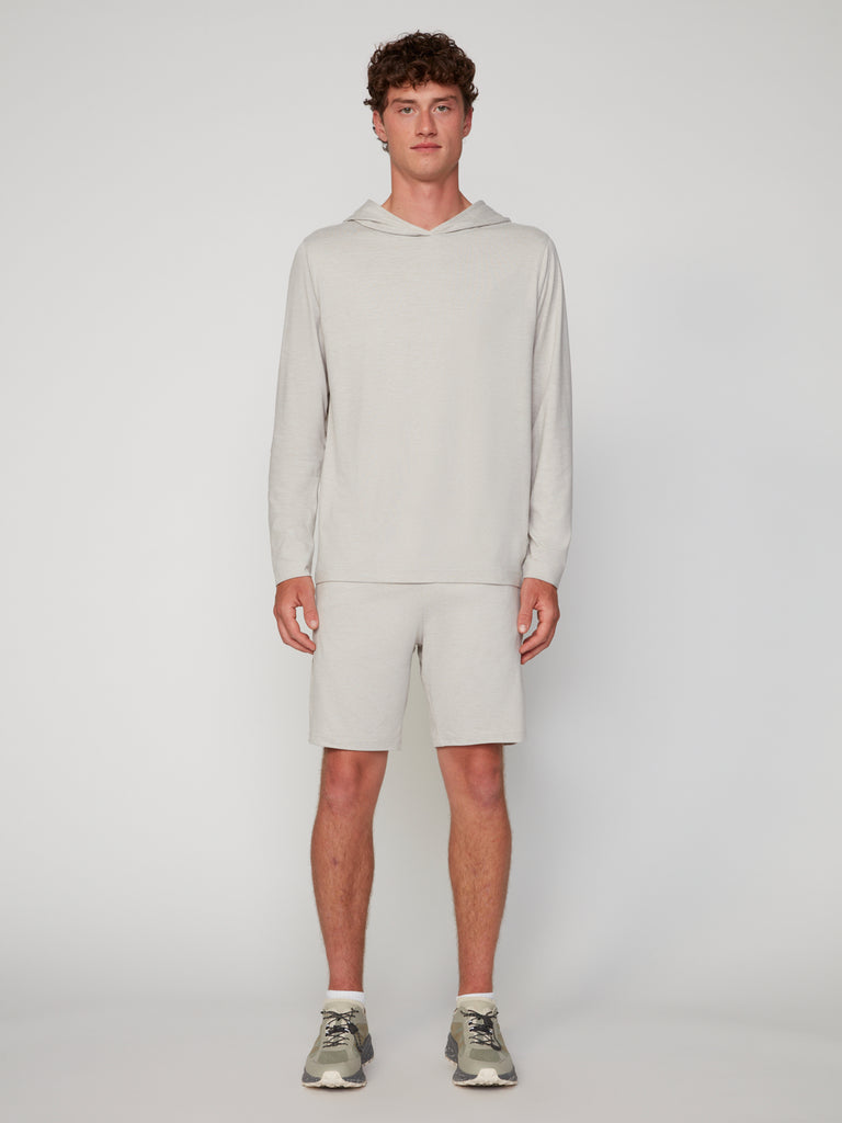 A young man stands facing forward, wearing a light gray hooded long-sleeve shirt and TECH APPAREL MEN’S SOFT:FLEX CLASSIC FIT PULL-ON KNIT SHORT - 8 INSEAM, paired with white socks and gray sneakers against a plain, light background.