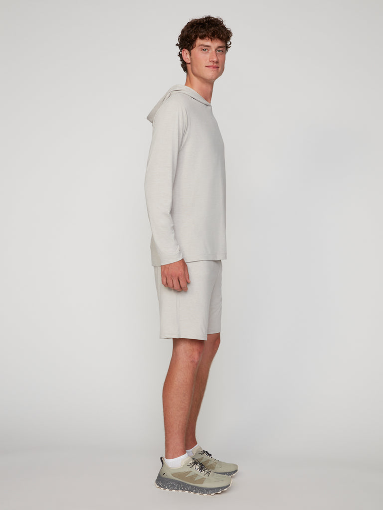 A young man in profile stands against a plain background, wearing a light gray hoodie, TECH APPAREL MEN’S SOFT:FLEX CLASSIC FIT PULL-ON KNIT SHORT - 8 INSEAM, and beige sneakers with gray soles.