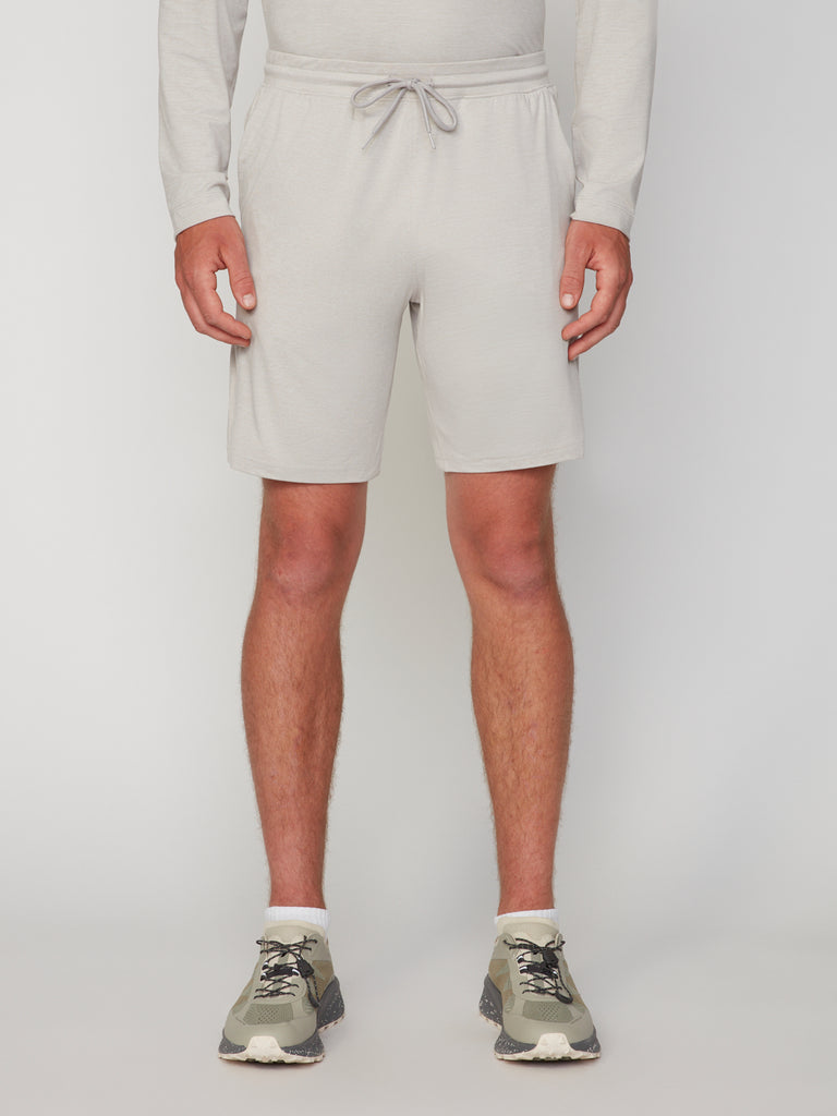 Wearing a light gray long-sleeve shirt and TECH APPAREL MEN’S SOFT:FLEX CLASSIC FIT PULL-ON KNIT SHORT - 8 INSEAM, with white socks and green sneakers, the person stands against a plain white background. Image is cropped above the shoulders.