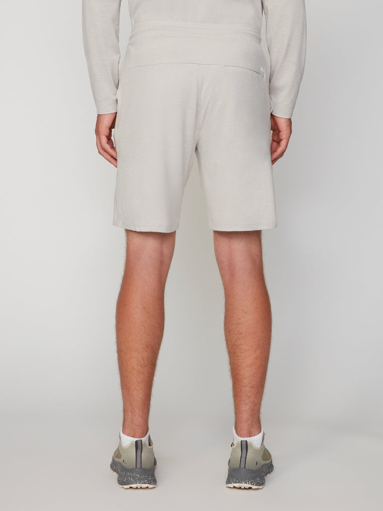 A man faces away, wearing a light beige long-sleeve top and TECH APPAREL MEN’S SOFT:FLEX CLASSIC FIT PULL-ON KNIT SHORT - 8 INSEAM in matching beige with gray athletic shoes. The background is plain white.