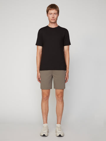A man stands facing forward against a plain light gray background, wearing a black t-shirt, white sneakers, and TECH APPAREL MEN’S FLEXLITE PULL-ON SHORT, 8 INSEAM. His arms rest naturally at his sides.